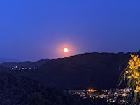 a full moon rises over a city with mountains in the background